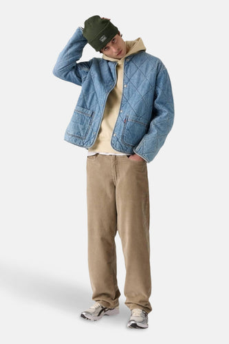 Man met groene muts, spijkerjas, hoodie, corduroy broek en sneakers.
