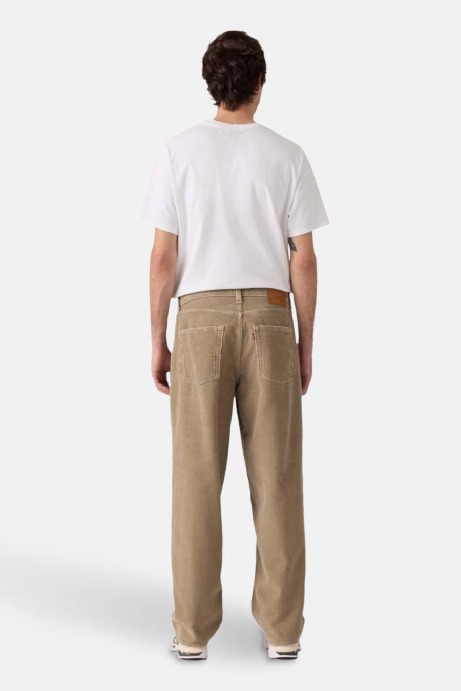 Man met witte T-shirt en beige corduroy broek, rug gezien.