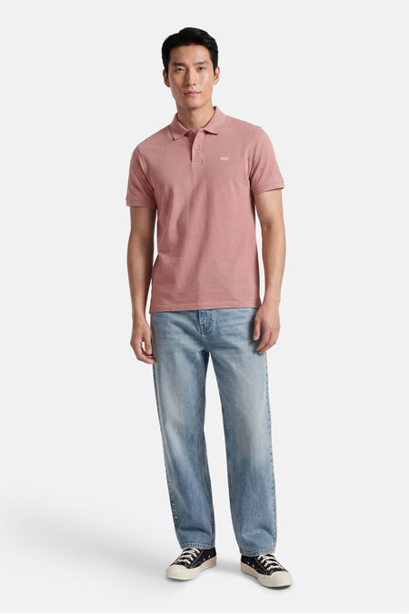 Polo rose Levi's® avec texture chinée, deux boutons et un petit logo ton sur ton, porté par un homme.