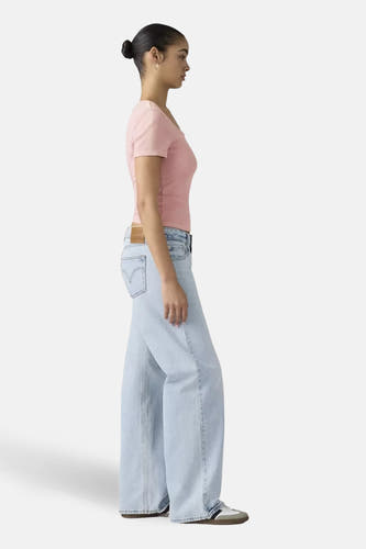 Wijd uitlopende jeans van lichtblauw denim van Levi's®, gecombineerd met een roze top en sneakers, in zij-aanzicht.