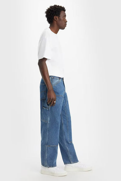 Jean en denim droit de Levi's, avec des poches et porté avec un T-shirt blanc et des baskets blanches, en vue latérale.