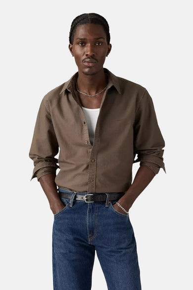 Chemise brune à longues manches de Levi's, avec col boutonné et portée sur un chemisier blanc, associée à un jeans foncé et une ceinture.