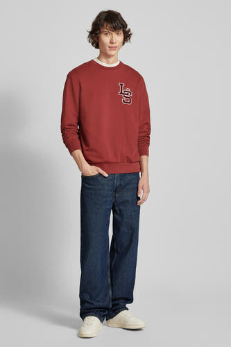 Jean bleu marine droit de Levi's, porté avec un pull rouge et des baskets blanches.