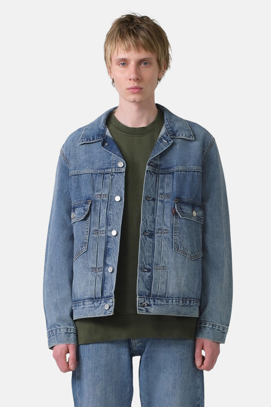 Man draagt denim jas en groene trui.
