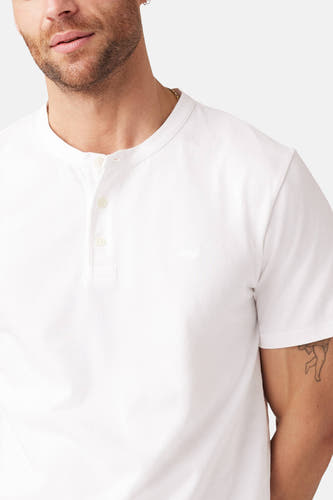 T-shirt blanc à manches courtes de Levi's®, avec une fermeture à boutons sur la ligne du cou et une petite tatouage sur le bras supérieur.