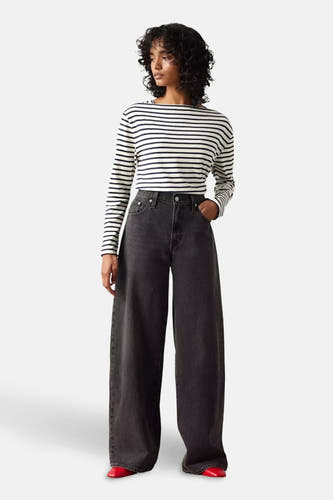 Jean droit noir de Levi's, porté avec un haut rayé et des chaussures rouges.