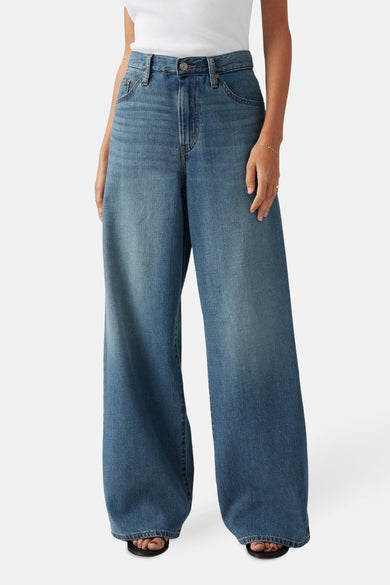 Jean droit en denim bleu de Levi's®, porté avec un modèle large, une chemise blanche et des sandales.