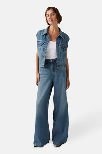 Jean droit en denim bleu moyen de Levi's, associé à un haut blanc et un gilet en denim.