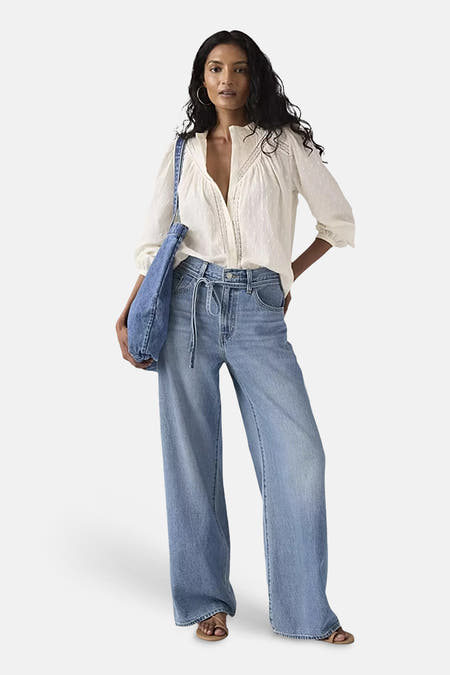 Blauwe straight jeans van Levi's, met koord in de taille, gecombineerd met een crèmekleurige blouse en een blauwe tas.
