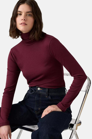 T-shirt Bordeaux à manches longues de Levi's, porté avec des jeans foncés et une chaise en argent sur un fond blanc.