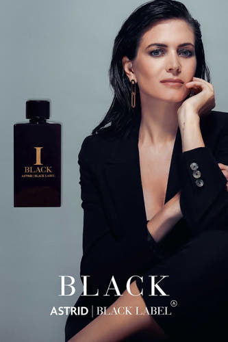 Parfum noir d'Astrid Black Label, à côté d'une femme en blazer noir avec des boucles d'oreilles dorées.