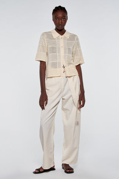 Gilet tricoté écru avec fermeture à boutons et manches courtes d'Astrid Black Label, motif rayé, modèle en vue de face portant un pantalon blanc et des sandales