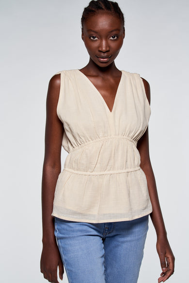 T-shirt beige d'Astrid Black Label, sans manches et avec des cordons à l'arrière, associé à des jeans bleus.