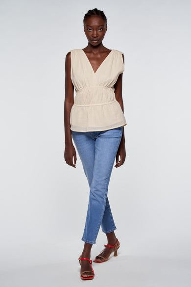T-shirt beige sans manches d'Astrid Black Label, porté avec des jeans et des sandales rouges.