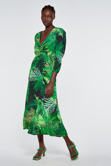 Robe verte à motif de feuilles tropicales d'Astrid Black Label, manches longues, col en V et jupe évasée, modèle en pied.