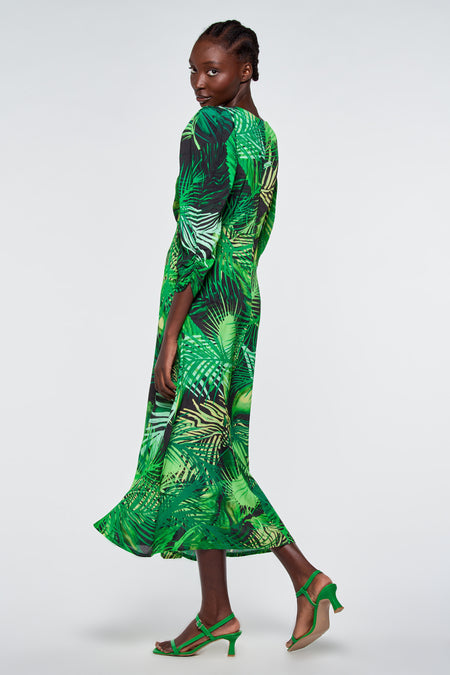 Robe verte à motif de feuilles tropicales d'Astrid Black Label, manches longues, texture soyeuse, modèle de profil avec des talons verts