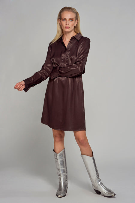 Manteau brun à longues manches d'Astrid Black Label, avec une ceinture et des chaussures argentées.