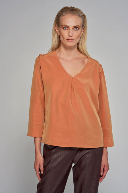 Blouse orange d'Astrid Black Label, avec un col V et des manches trois-quarts, portée par une femme blonde avec un ombre à paupières orange.