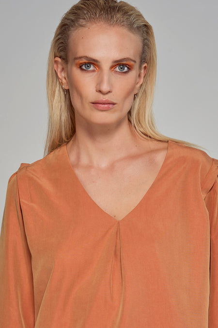 Oranje blouse van Astrid Black Label, met een V-hals en driekwart mouwen, gedragen door een blonde vrouw met oranje oogschaduw.

