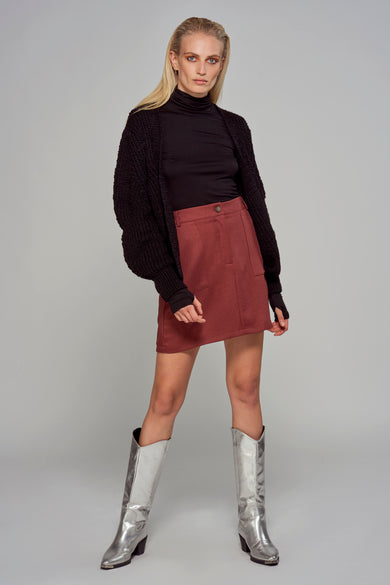 Gilet noir d'Astrid Black Label, porté sur une veste noire et une jupe rouge, avec des bottes argentées.