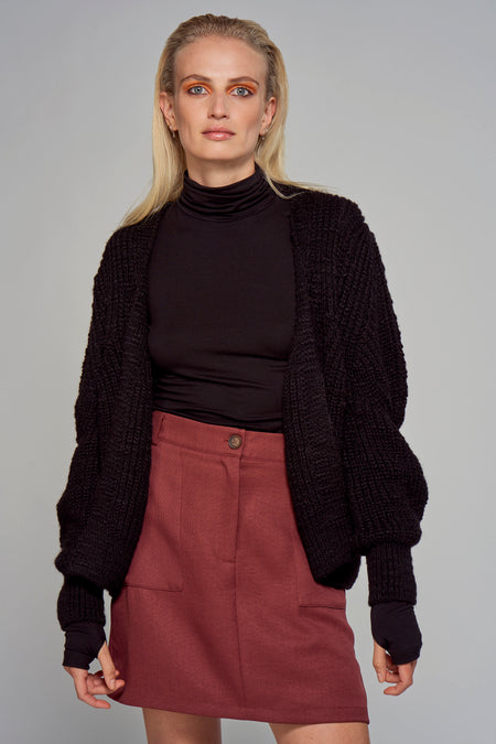 Zwart gilet van Astrid Black Label, met brede gebreide textuur, gedragen over een zwarte coltrui en een rode rok.
