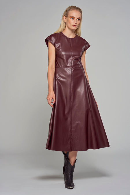 Robe sans manches en imitation cuir bordeaux d'Astrid Black Label, avec une jupe qui tombe et portée avec des bottes noires.