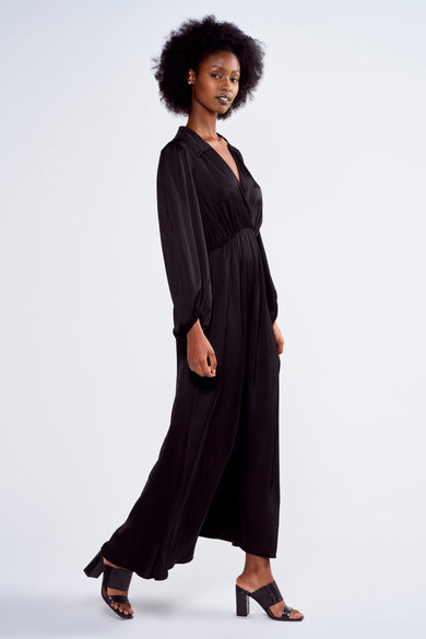Robe noire à longues manches d'Astrid Black Label, en tissu brillant et portée avec des talons ouverts.