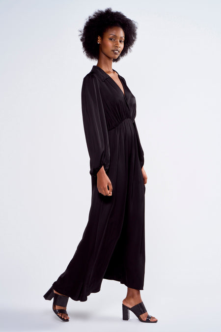 Robe noire à longues manches d'Astrid Black Label, en tissu brillant et portée avec des talons ouverts.