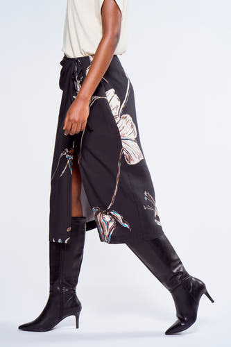 Robe noire à motif floral d'Astrid Black Label, avec une encolure dégagée et associée à des bottes noires à talon.