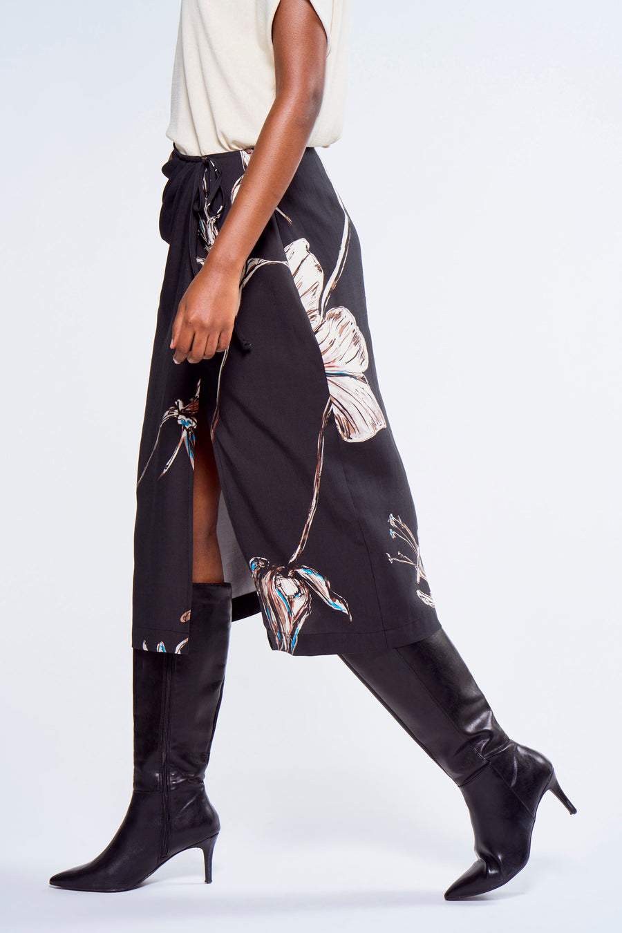 Robe noire à motif floral d'Astrid Black Label, avec une encolure dégagée et associée à des bottes noires à talon.