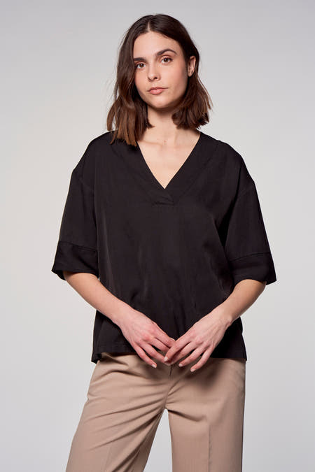 Blouse noire à manches courtes d'Astrid Black Label, vue de derrière, associée à un pantalon beige.