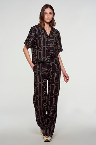 Vrouw in bruine pyjama-achtige set met geometrische print staand.