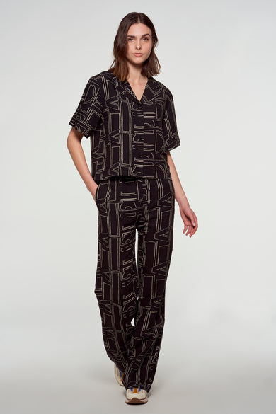 Zwarte broek van Astrid Black Label met opvallend patroon, gecombineerd met bijpassende blouse en witte sneakers.
