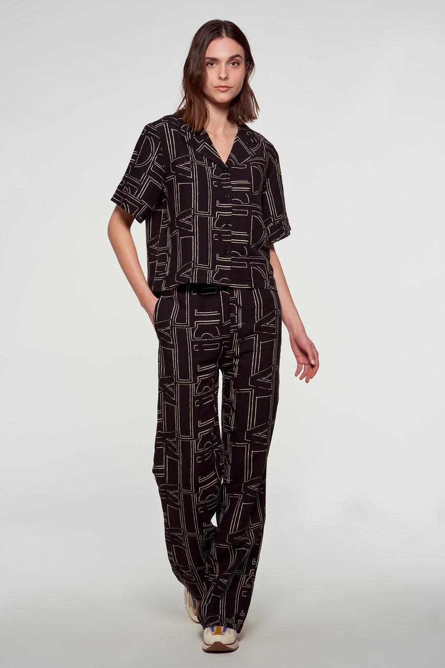 Vrouw in bruine pyjama-achtige set met geometrische print staand.