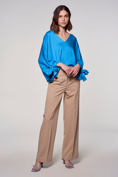 Blouse bleue d'Astrid Black Label, avec des manches longues et des détails à carreaux, associée à un pantalon kaki et des baskets bleues.