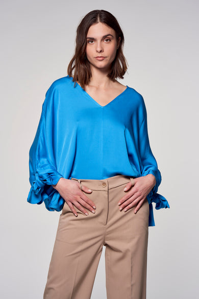 Blouse bleue Astrid Black Label avec des manches longues et des détails rayés, associée à un pantalon beige.