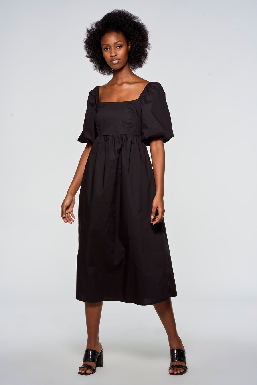 Zwarte jurk met pofmouwen en vierkante halslijn, gedragen door een model met afro haar.