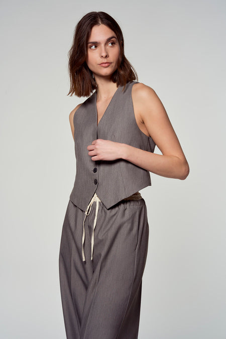 Blazer gris d'Astrid Black Label, avec col V et fermeture à boutons, associé à un pantalon coordonné avec cordon de serrage.