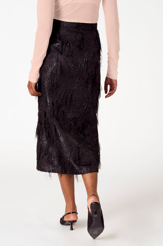 Vrouw, lange mouwen roze top, zwarte rok met franjes, zwarte pumps.
