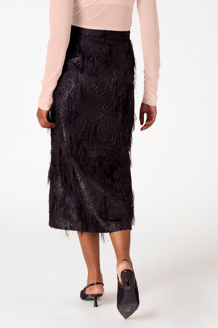 Vrouw, lange mouwen roze top, zwarte rok met franjes, zwarte pumps.
