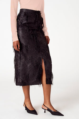 Vrouw in zwarte rok met split en hakken, witte achtergrond.