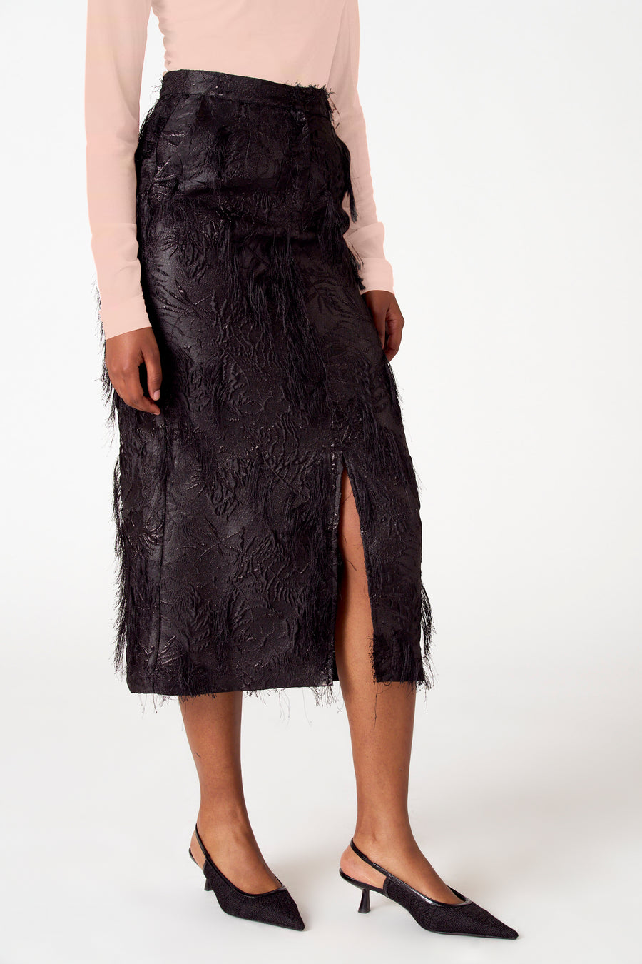 Vrouw in zwarte rok met split en hakken, witte achtergrond.