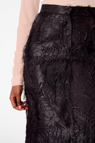 Close-up van een zwarte rok met textuur en lange, gerafelde details, gedragen met een lichtroze blouse.