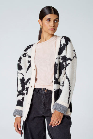 Gilet écru d'Astrid Black Label, avec un motif noir et porté sur une chemise rose clair et un pantalon noir.