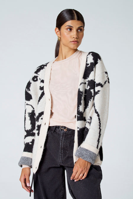 Gilet écru d'Astrid Black Label, avec un motif noir et porté sur une chemise rose clair et un pantalon noir.