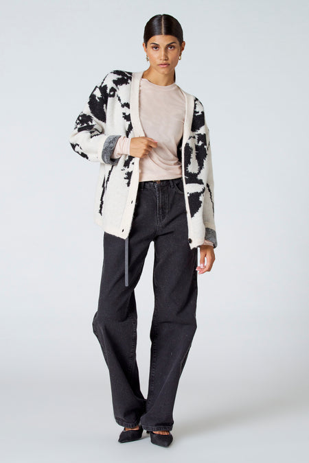 Gilet écru d'Astrid Black Label, avec un motif noir frappant, porté sur une chemise rose et des jeans foncés.