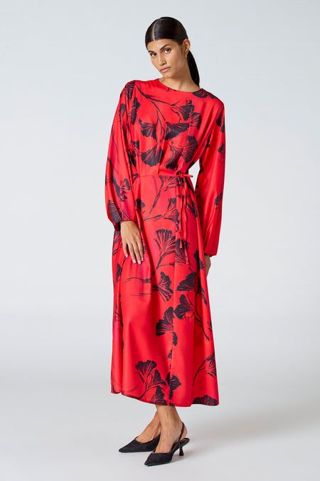 Robe rouge à longues manches d'Astrid Black Label, avec un motif de feuille foncé et une ceinture élastique.