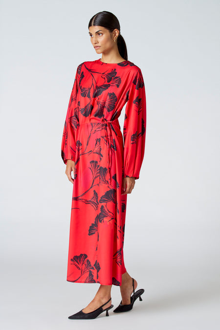 Robe rouge à longues manches d'Astrid Black Label, avec des motifs de fleurs noires et une ceinture coordonnée.