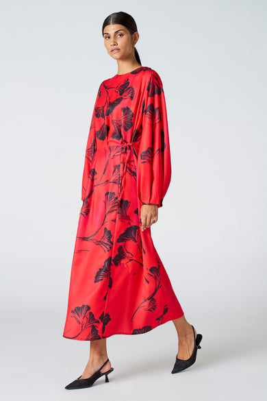 Robe rouge à longues manches d'Astrid Black Label, avec imprimé de fleurs noires et talons compensés noirs.