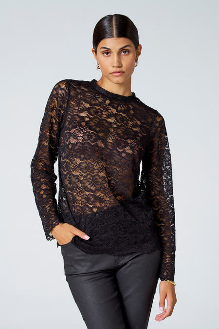 Blouse noire à manches longues d'Astrid Black Label, avec un motif floral sur les bords et associée à une jupe noire et des boucles d'oreilles dorées.